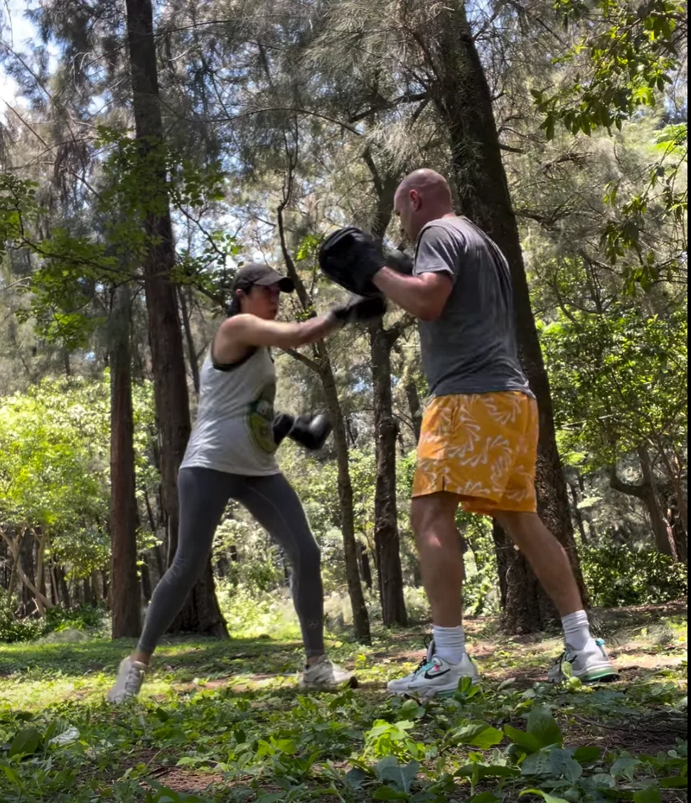 A client throws a punch into the coach's focus mitts during an outdoor pad-work session.